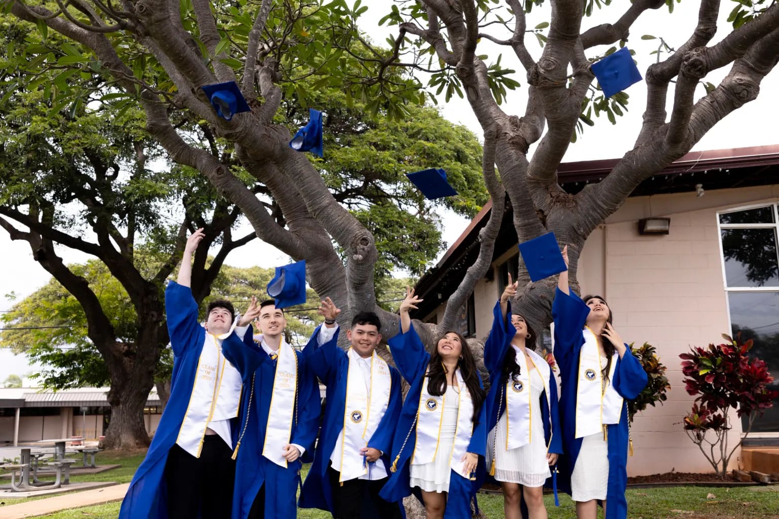Kapolei Christian Academy graduates tossing their caps under the campus tree.